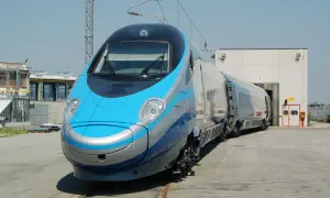 Niebiesko-srebrny pociąg Pendolino na torach przed budynkiem.