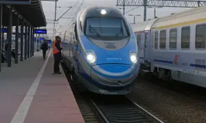 Pendolino na dworcu, obok niego stoi pracownik kolei w kamizelce.