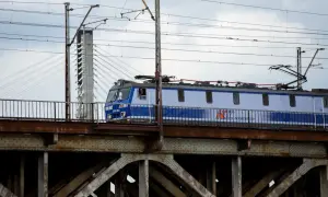 Niebiesko-biały pociąg PKP Intercity przejeżdża przez zardzewiały most kolejowy.