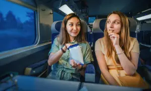 Dwie kobiety jedzą przekąski w pociągu intercity, patrząc przez okno.