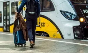 Podróżny z walizką i kurtką idzie w stronę pociągu KD. Rozkład PKP czeka na pasażerów.