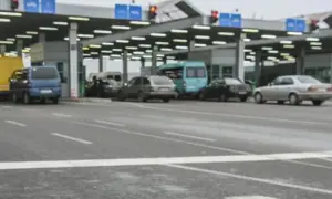 Kolejka samochodów na granicy polsko rosyjskiej. Widać budynki przejścia granicznego, sygnalizację świetlną i różne pojazdy.