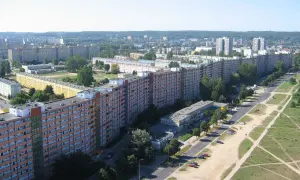 Długi, falisty budynek mieszkalny, znany jako Falowiec Gdańsk, rozciąga się na tle zielonych wzgórz i innych bloków.