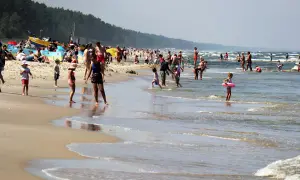 Tłum ludzi cieszy się słońcem i kąpielą w najcieplejszej wodzie w Bałtyku. Dzieci bawią się na plaży i w morzu, dorośli odpoczywają.
