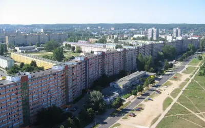Długi, falisty budynek mieszkalny, znany jako Falowiec Gdańsk, rozciąga się na tle zielonych wzgórz i innych bloków.