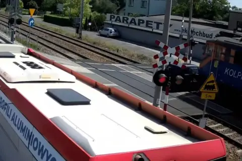Autobus czeka na przejazd kolejowy w drodze do Częstochowy. Pociąg Kolprem mija przejazd.