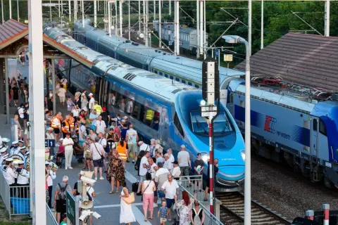Tłum ludzi na peronie czeka na pociąg Pendolino. Widoczne są różne trasy kolejowe i nowoczesne składy.