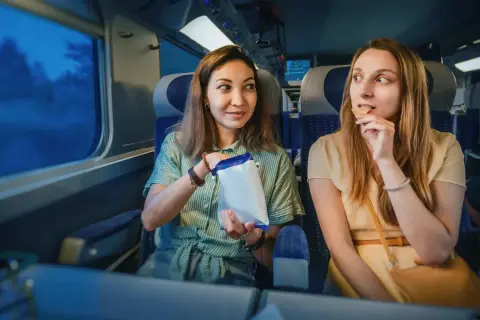 Dwie kobiety jedzą przekąski w pociągu intercity, patrząc przez okno.