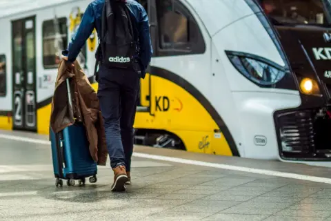 Podróżny z walizką i kurtką zmierza na peron, gdzie czeka łódź Władysławowo.