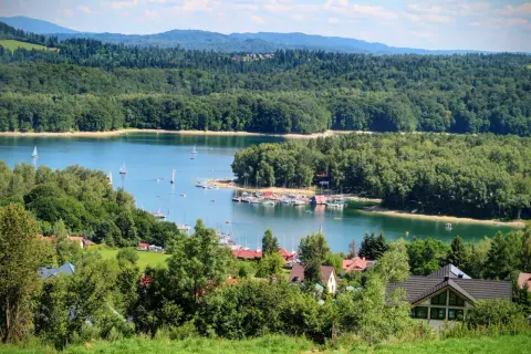 Malowniczy widok na Jezioro Solińskie z żaglówkami i lasami. Idealne miejsce, by sprawdzić, jak dojechać nad Solinę samochodem i odpocząć.