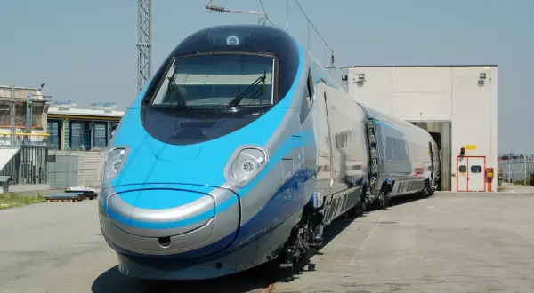 Niebiesko-srebrny pociąg Pendolino na torach przed budynkiem.