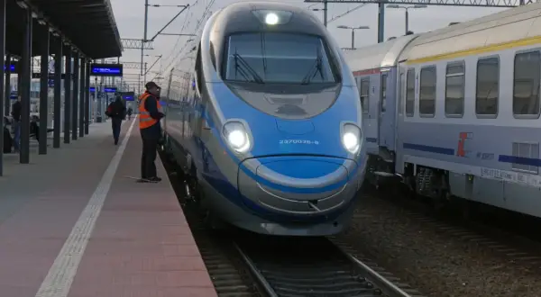 Pendolino na dworcu, obok niego stoi pracownik kolei w kamizelce.
