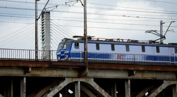 Niebiesko-biały pociąg PKP Intercity przejeżdża przez zardzewiały most kolejowy.
