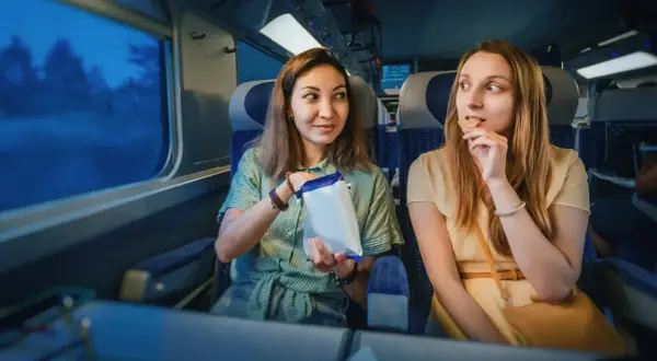 Dwie kobiety jedzą przekąski w pociągu intercity, patrząc przez okno.