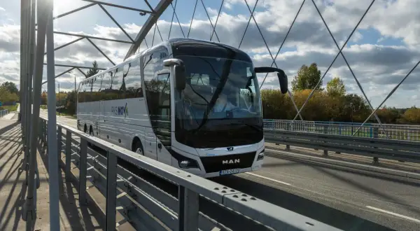 Autobus PKS NOVA na moście, podróżujący z Grajewa do Augustowa. Słoneczny dzień, chmury na niebie.