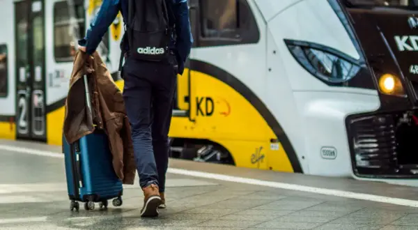 Podróżny z walizką i kurtką zmierza na peron, gdzie czeka łódź Władysławowo.