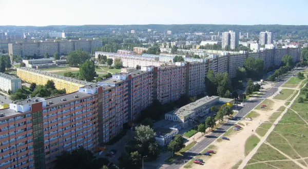 Długi, falisty budynek mieszkalny, znany jako Falowiec Gdańsk, rozciąga się na tle zielonych wzgórz i innych bloków.