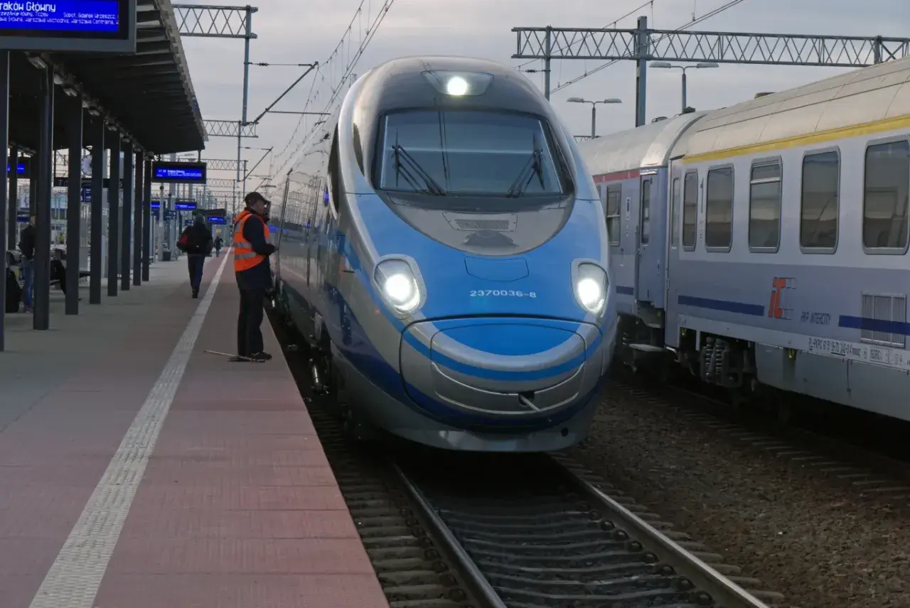 Pendolino na dworcu, obok niego stoi pracownik kolei w kamizelce.