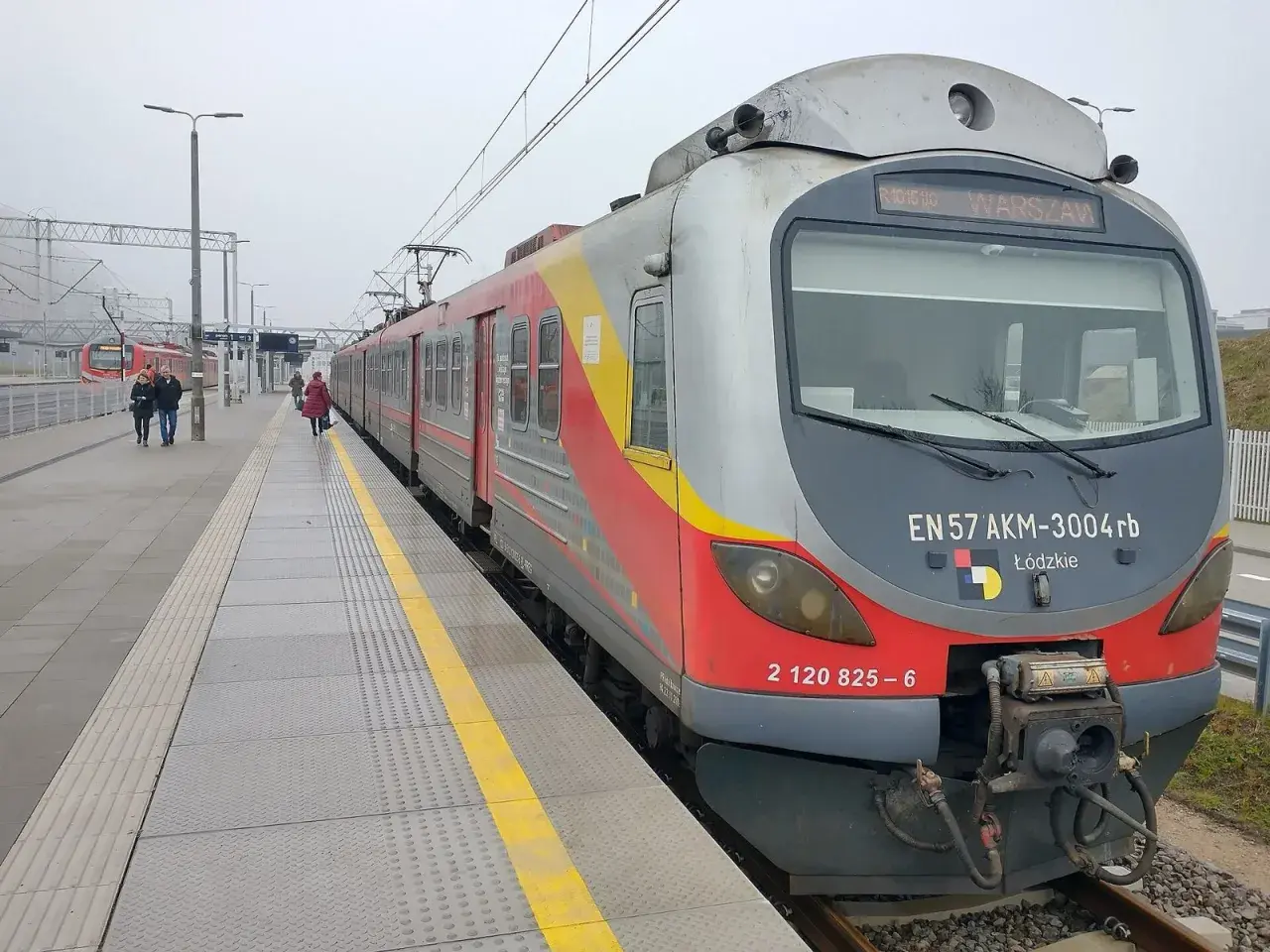 Pociąg EN57 AKM-3004rb z napisem "WARSZAWA" na stacji. Sprawdź rozkład jazdy Nowy Dwór Mazowiecki, aby zaplanować podróż.