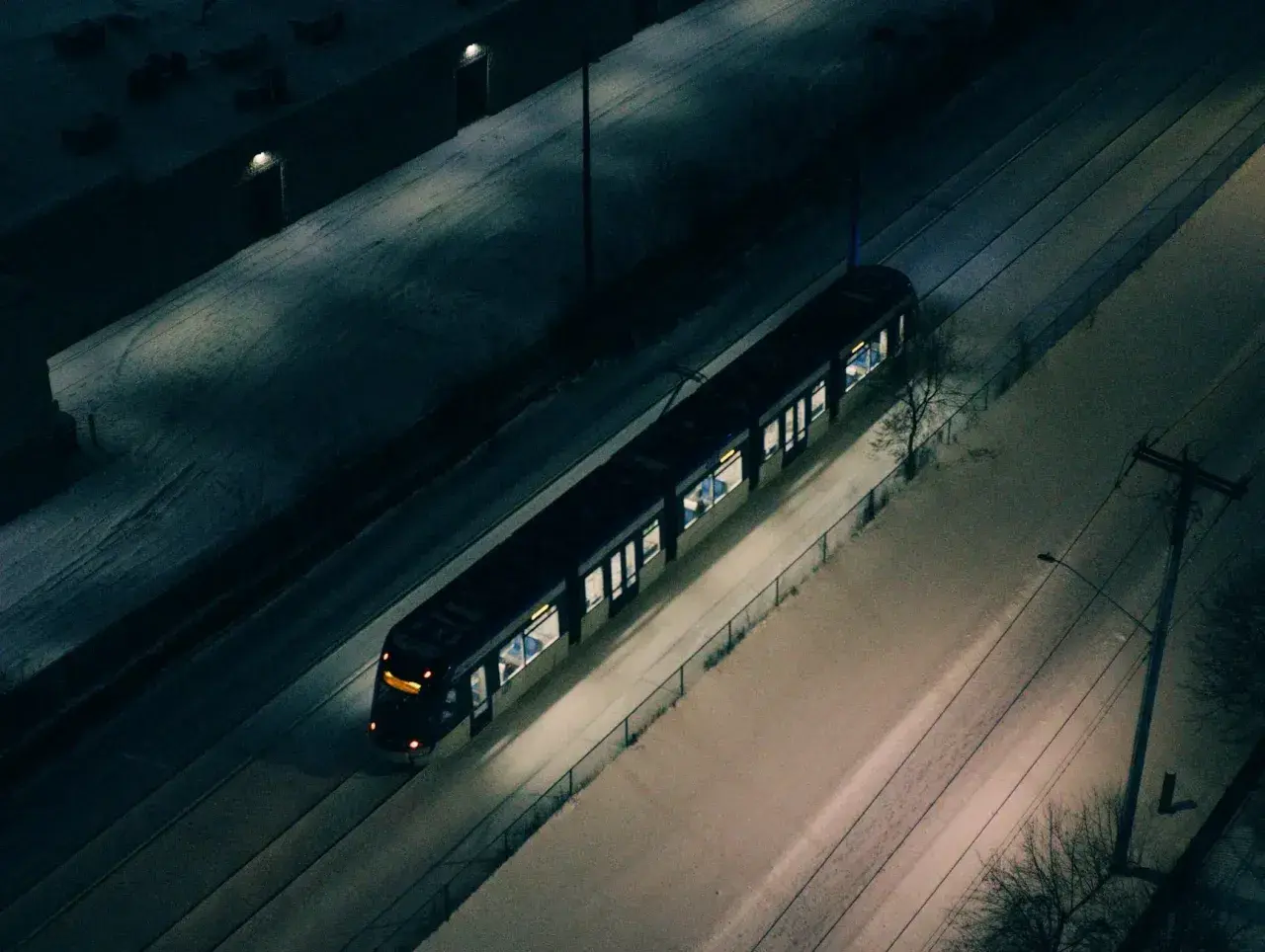 Pociąg Warszawskiej Kolei Dojazdowej mija ośnieżone tereny nocą.
