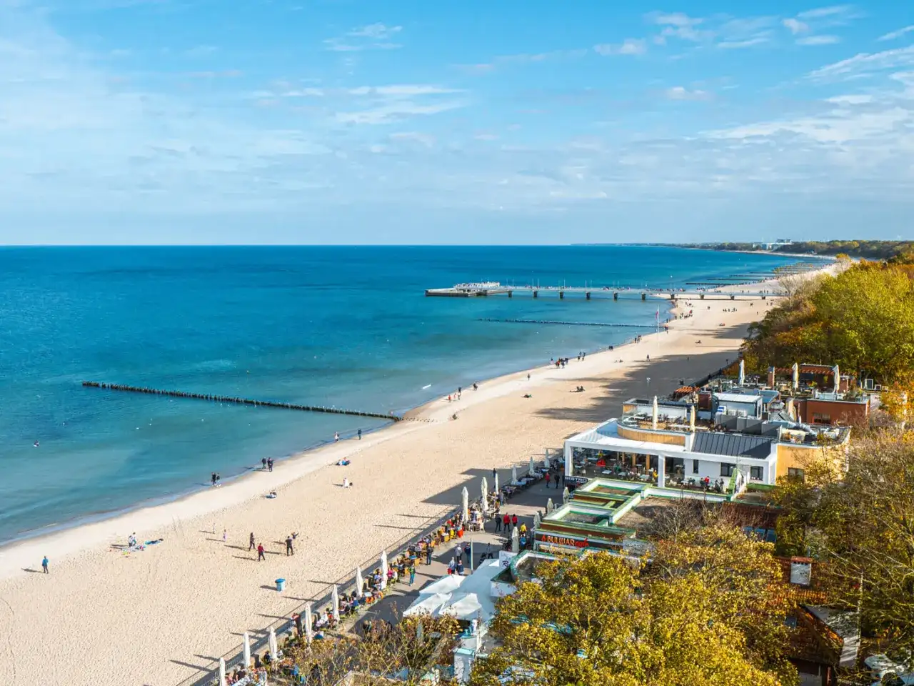Piękna plaża i molo w jednej z nadmorskich miejscowości. Ludzie spacerują, odpoczywają, ciesząc się jesiennym słońcem.