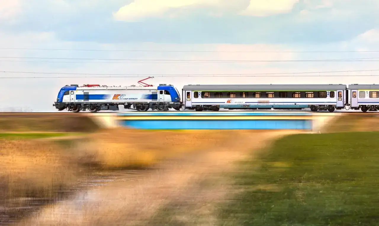 Pociąg Intercity pędzi po torach, łącząc Białystok z Lublinem. Rozmyte krajobrazy i błękitny most tworzą dynamiczną scenę.