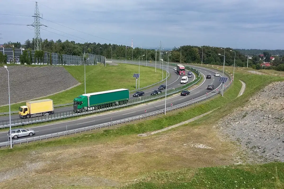 Droga ekspresowa koło Kęt Wrocław. Ciężarówki i samochody jadą po wielopasmowej trasie wśród zieleni i słupów energetycznych.