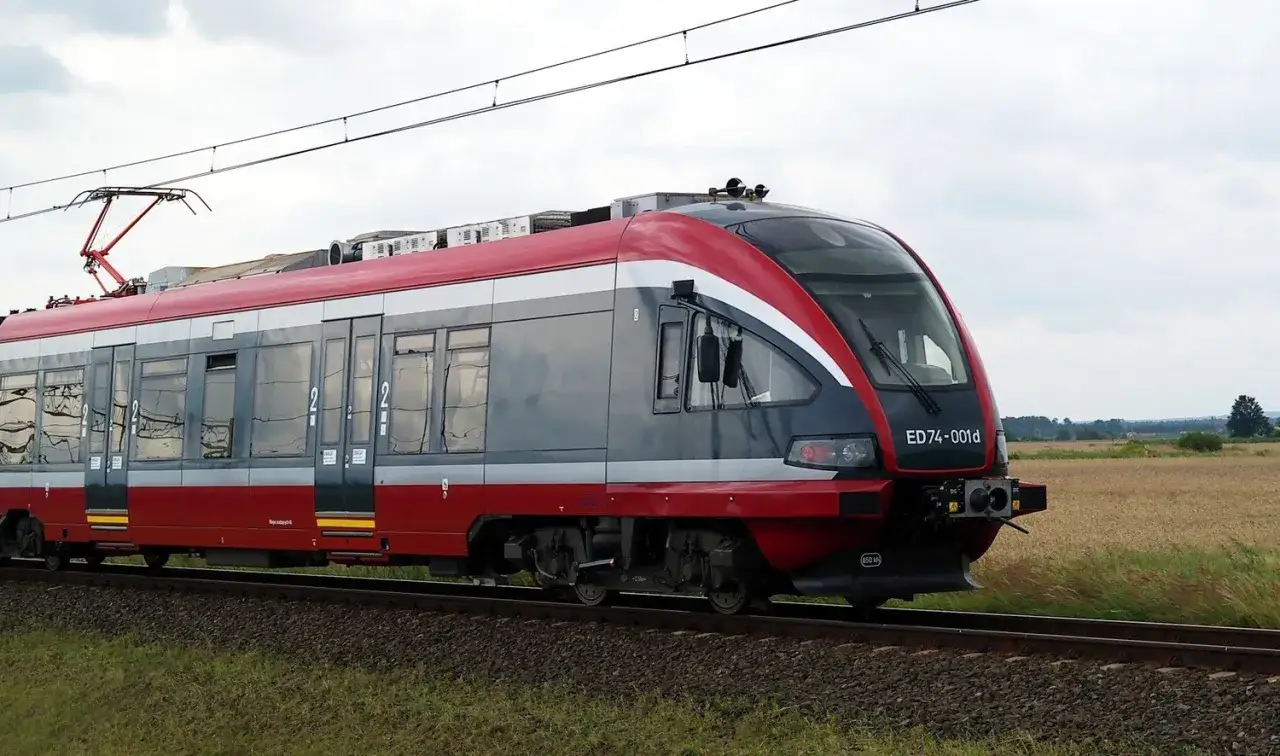 Nowy pociąg ED74-001d, czerwono-szary, przemierza pola.