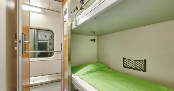 Wnętrze wagonu sypialnego z dwupoziomową kuszetką. Po lewej drzwi do przedziału, po prawej zielona pościel na dolnej kuszetce.