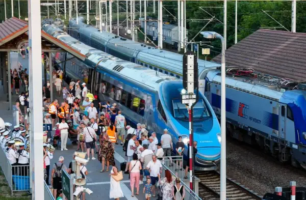 Tłum ludzi na peronie czeka na pociąg Pendolino. Widoczne są różne trasy kolejowe i nowoczesne składy.