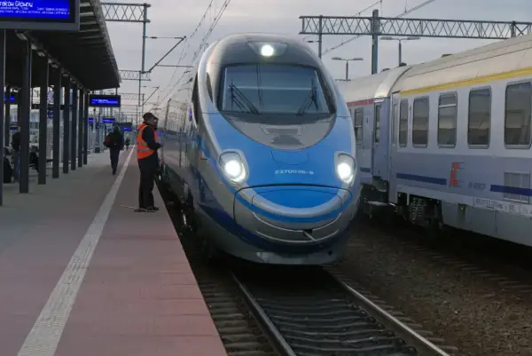Pendolino na dworcu, obok niego stoi pracownik kolei w kamizelce.