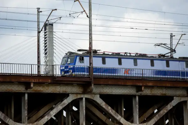 Niebiesko-biały pociąg PKP Intercity przejeżdża przez zardzewiały most kolejowy.