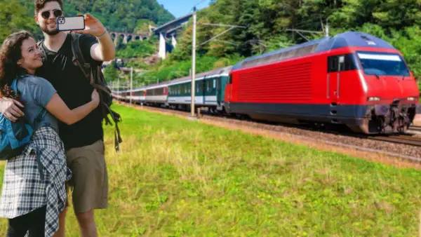 Para podróżuje obok torów, na których mija ich czerwony pociąg.