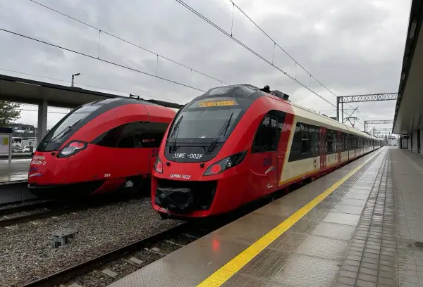 Dwa czerwone pociągi SKM stojące na peronie.