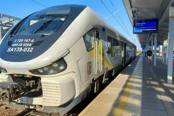 Pociąg SA139-032 na stacji, gotowy do odjazdu. Na tablicy informacyjnej widnieje kierunek Guben. Zielona góra łódź to symbol, który może kojarzyć się z podróżą.