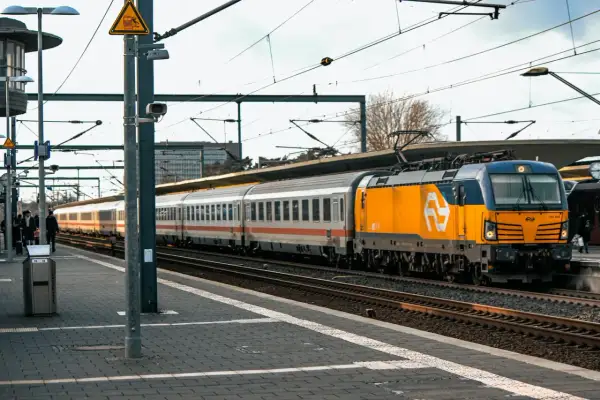 Pociąg z żółtą lokomotywą stoi na stacji, pasażerowie czekają, być może z powodu opóźnienia.